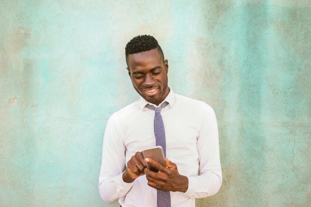 A well-dressed man engaging with his smartphone against a textured blue wall.