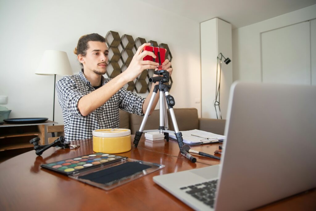 A male vlogger adjusts his camera on a tripod, preparing for a video shoot in a stylish home studio.