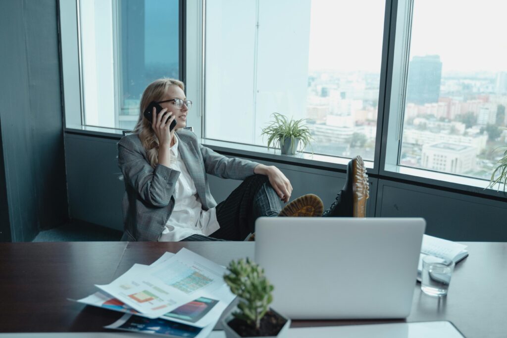 A confident businesswoman makes a phone call in a modern office with city views.