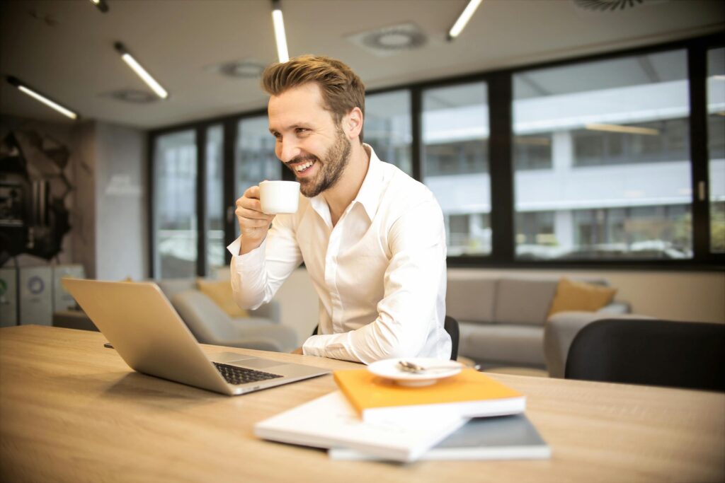 pexels-photo-927451-927451 Man enjoying a coffee break while working in a modern office with laptop and books.